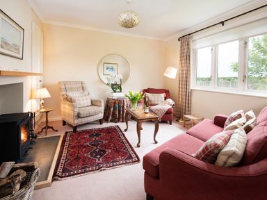 A living room with red couches a plaid armchair a wooden coffee table and a fireplace at Barmoor Ridge in Lowick near Holy Island