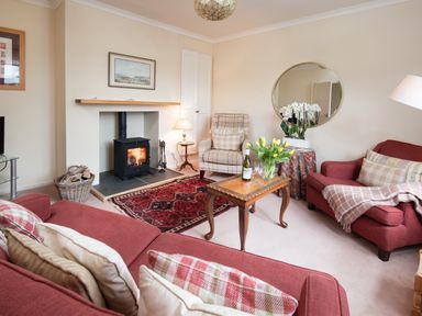 A living room with red sofas a wooden coffee table and a lit fireplace at Barmoor Ridge in Lowick near Holy Island