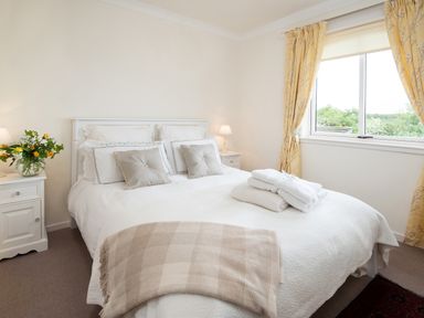 A bedroom with a double bed pillows folded towels bedside tables lamps flowers and yellow curtains at Barmoor Ridge in Lowick near Holy Island