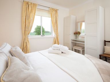 A bedroom with a made bed with towels on it yellow curtains wardrobe and a dressing table at Barmoor Ridge Lowick near Holy Island
