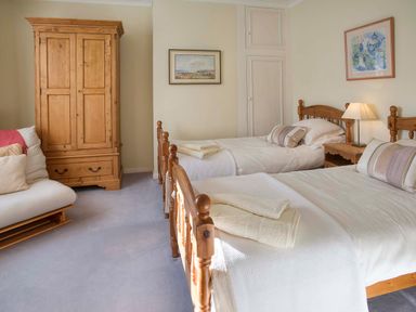A bedroom with two single beds a wooden wardrobe a sofa and framed pictures at Barmoor Ridge in Lowick near Holy Island