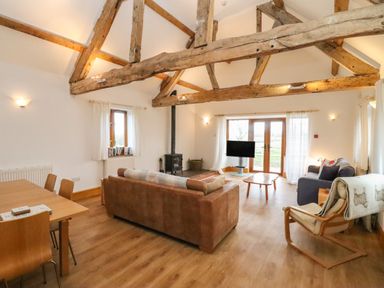 A living room with wooden beams a brown sofa a blue armchair a wooden dining table and chairs and a wood stove at Hill Farm Cottage in Kerrys Gate near Abbey Dore