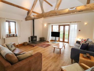 A living room with wooden beams a fireplace two sofas a coffee table a television and large windows at Hill Farm Cottage Kerry's Gate near Abbey Dore