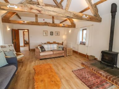 A living room with wooden beams a wood stove a sofa and armchairs at Hill Farm Cottage Kerry's Gate near Abbey Dore