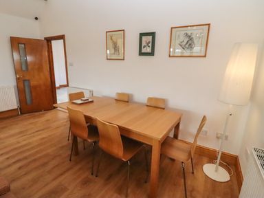 A dining room with a wooden table six chairs floor lamp and framed pictures on the wall at Hill Farm Cottage Kerry's Gate near Abbey Dore