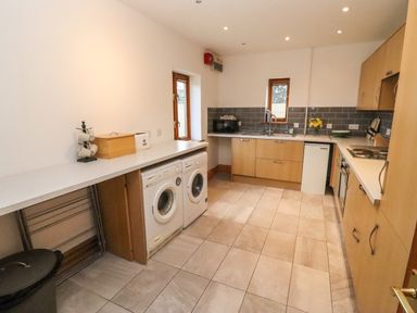 A kitchen with tiled floor wooden cabinets washing machine dishwasher microwave and sink at Hill Farm Cottage Kerry's Gate near Abbey Dore