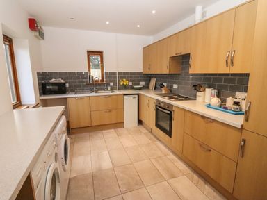 A kitchen with wooden cabinets a washing machine a microwave and a built in oven at Hill Farm Cottage Kerry's Gate near Abbey Dore
