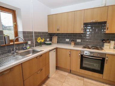 A kitchen with wooden cabinets a stainless steel sink electric stove and oven and grey tiled backsplash at Hill Farm Cottage Kerry's Gate near Abbey Dore
