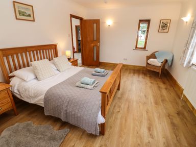 A bedroom with a wooden bed and bedside tables a chair near a window and pictures on the walls at Hill Farm Cottage in Kerrys Gate near Abbey Dore