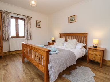 A bedroom with a wooden double bed two bedside tables with lamps window with curtains and wooden wardrobe at Hill Farm Cottage Kerry's Gate near Abbey Dore
