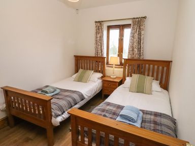 A bedroom with two single beds a wooden nightstand with a lamp and a window with curtains at Hill Farm Cottage Kerry's Gate near Abbey Dore