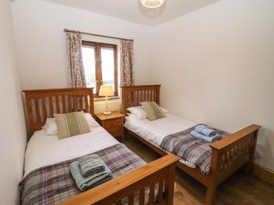 A bedroom with two single wooden beds a nightstand with a lamp and a window with curtains at Hill Farm Cottage in Kerrys Gate near Abbey Dore