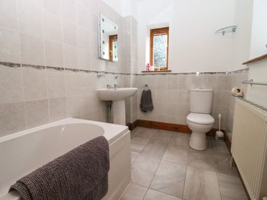 A bathroom with a bathtub a towel a sink a mirror a window a toilet a toilet brush and a radiator at Hill Farm Cottage Kerry's Gate near Abbey Dore