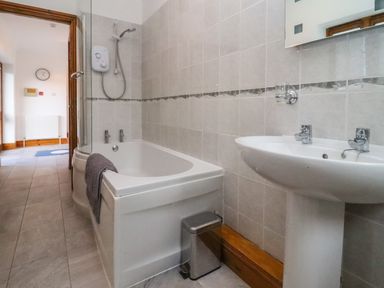 A bathroom with a bathtub shower sink mirror and small trash bin at Hill Farm Cottage in Kerrys Gate near Abbey Dore