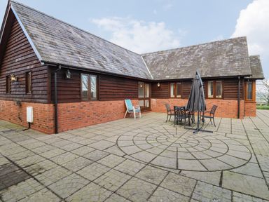 An outdoor patio with circular stone pattern and metal table with chairs and umbrella next to a brick and wood building at Hill Farm Cottage Kerry's Gate near Abbey Dore