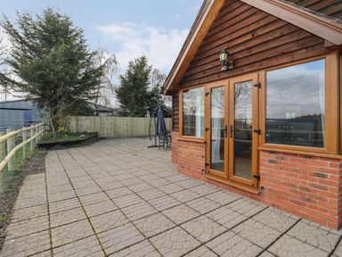 An outdoor patio area with paved flooring wooden fence and a wooden house with glass doors and windows at Hill Farm Cottage in Kerrys Gate near Abbey Dore