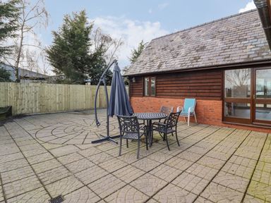 An outdoor patio with a round metal table four chairs a closed umbrella and a wooden and brick building at Hill Farm Cottage in Kerrys Gate near Abbey Dore