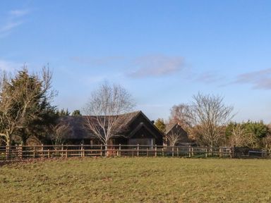 A grassy field with a wooden fence and trees around a cottage at Hill Farm Cottage in Kerrys Gate near Abbey Dore
