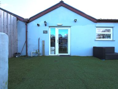 An exterior view of a blue building with a glass door and a window on a lawn area at Dylans Court in Laugharne