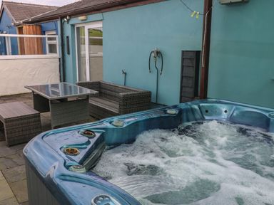 A patio area with a hot tub and outdoor wicker furniture at Barn Cottage in Laugharne