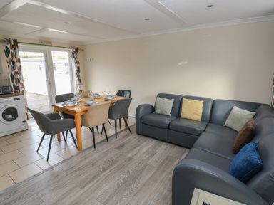 A dining area with a wooden table set for six and a dark sectional sofa with cushions at Barn Cottage in Laugharne