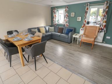 A dining area with a wooden table and six chairs next to a living room with a corner sofa and an armchair at Barn Cottage in Laugharne