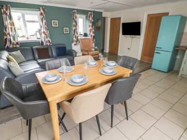 A dining table set with plates bowls and glasses in an open plan kitchen with chairs a large sofa armchair and a turquoise fridge at Barn Cottage in Laugharne