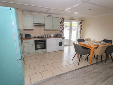 A kitchen with green cabinets a blue refrigerator a wooden dining table set with dishes and wine glasses and double glass doors at Barn Cottage in Laugharne