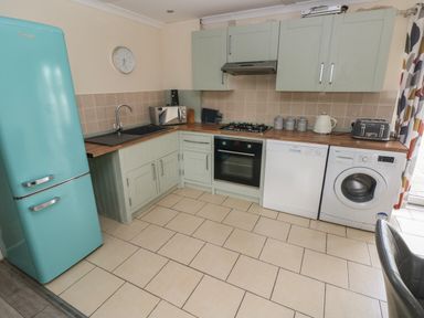 A kitchen with a blue fridge sink microwave oven dishwasher washing machine and countertop appliances at Barn Cottage in Laugharne