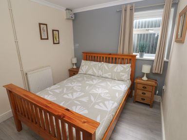 A bedroom with a wooden bed and bedside tables with lamps and a window with curtains at Barn Cottage in Laugharne
