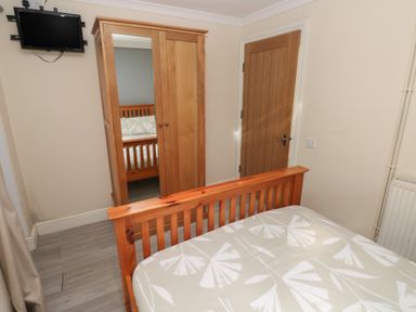 A bedroom with a wooden bed frame a wardrobe with mirrored door a wall mounted television and a wooden door at Barn Cottage in Laugharne