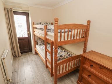 A small bedroom with wooden bunk beds a wooden chest of drawers and a door with a curtain at Barn Cottage in Laugharne