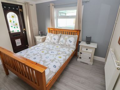 A bedroom with a wooden bed white floral bedding two white bedside tables with lamps a stained glass door and a window at Barn Cottage in Laugharne