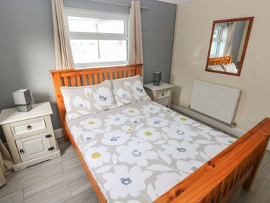 A bedroom with a wooden bed with floral bedding two bedside tables with lamps a window and a wall mirror at Barn Cottage in Laugharne
