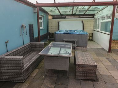 A covered patio area with wicker furniture and a hot tub at Barn Cottage in Laugharne