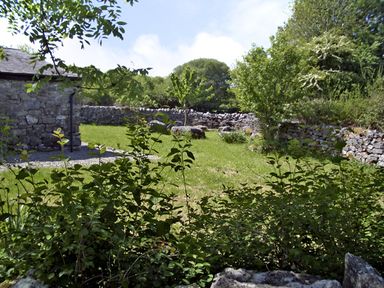 A garden with green grass trees bushes stone walls and a stone building at Clooncorraun Cottage in Ballinrobe County Mayo