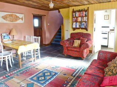 A living room with patterned sofas a wooden table with chairs a carpet on a stone floor and a bookshelf at Clooncorraun Cottage in Ballinrobe County Mayo