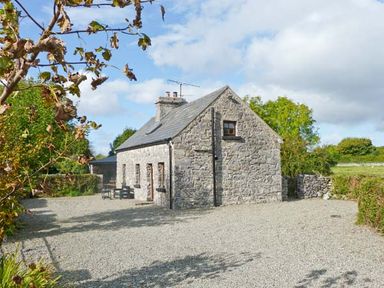 A stone cottage with a slate roof surrounded by bushes and gravel at Clooncorraun Cottage in Ballinrobe County Mayo