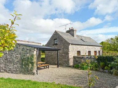 A stone cottage with a covered outdoor seating area and gravel yard at Clooncorraun Cottage in Ballinrobe County Mayo