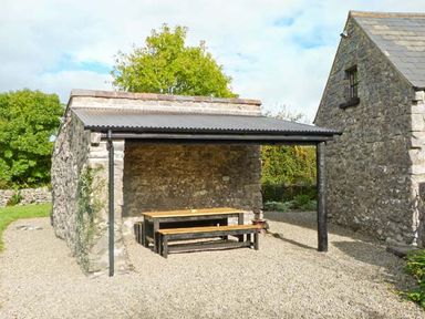 A stone outdoor shelter with a wooden table and benches at Clooncorraun Cottage in Ballinrobe County Mayo