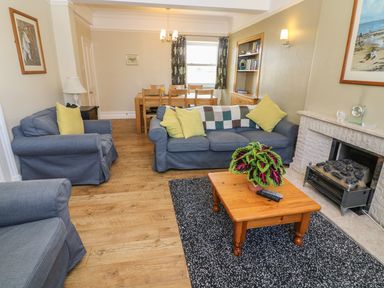 A living room with blue sofas yellow cushions a wooden coffee table with a plant and a dining table at Riverside View in Cark in Cartmel