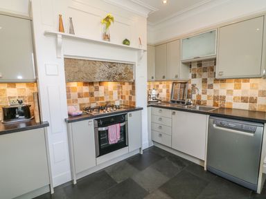 A kitchen with grey cabinets tiled backsplash and appliances at Riverside View in Cark in Cartmel