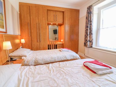 A bedroom with two single beds wooden wardrobes and a window with curtains at Riverside View in Cark in Cartmel