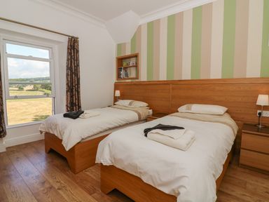 A bedroom with two single beds wooden furniture and a window with curtains at Riverside View in Cark in Cartmel