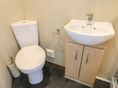 A bathroom with a white toilet and a white sink with a wooden cabinet at Riverside View in Cark in Cartmel
