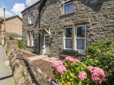 The stone exterior of a house with a white door wooden bench and pink flowers at Riverside View in Cark in Cartmel