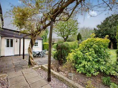 A backyard patio with a table and chairs near a white house and garden plants at Ingleside in Adsett Royal Forest of Dean