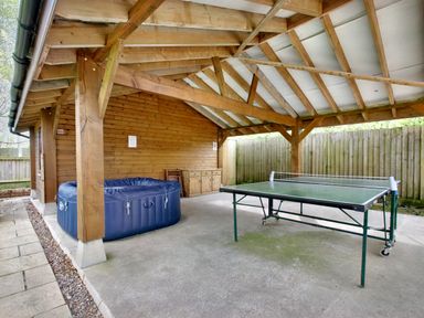 An outdoor covered area with a ping pong table a blue inflatable hot tub and wooden furniture at Ingleside in Adsett Royal Forest of Dean