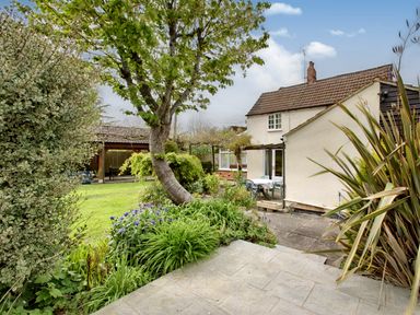 A garden with plants trees a paved patio and a white house with a brown tiled roof at Ingleside in Adsett Royal Forest of Dean