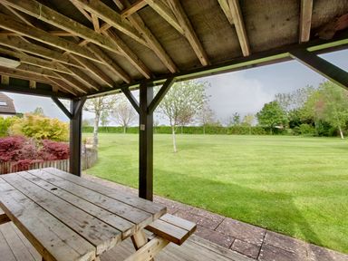 A covered wooden picnic table under a wooden shelter overlooking a grassy garden with trees at Ingleside in Adsett Royal Forest of Dean
